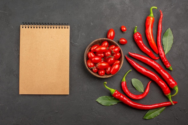 Vue de dessus les poivrons rouges et payer les feuilles et un bol de tomates cerises et un cahier sur tableau noir