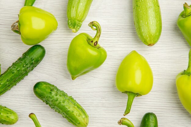 Vue de dessus des poivrons verts frais avec des concombres verts et des tomates sur un bureau blanc couleur salade mûre repas photo chaud