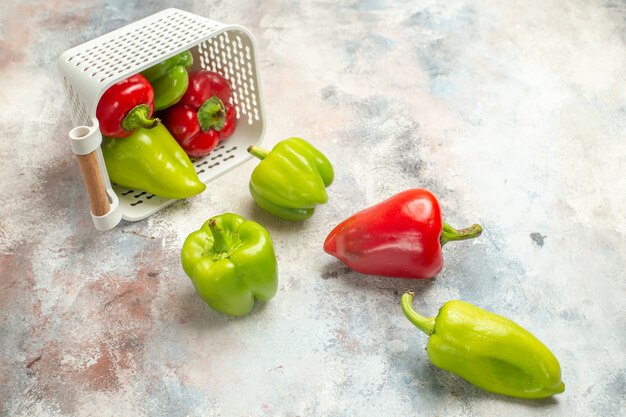 Vue de dessus poivrons verts et rouges dispersés dans un panier en plastique sur une surface nue avec un espace libre