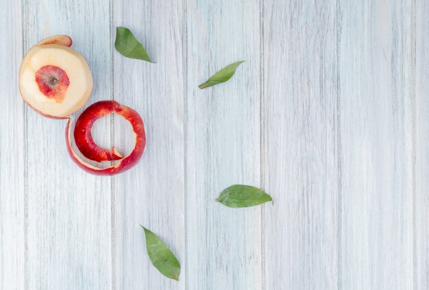 Vue de dessus de la pomme rouge et sa coquille sur fond de bois décoré de feuilles avec espace copie