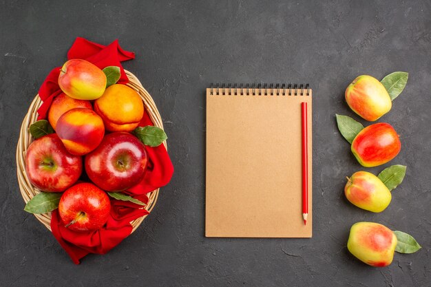 Vue de dessus des pommes fraîches avec des pêches à l'intérieur du panier sur la table sombre des fruits frais mûrs