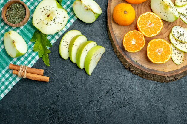 Vue de dessus des pommes et des mandarines coupées sur des bâtons de cannelle ronds rustiques attachés avec une corde sur une nappe verte sur une table sombre