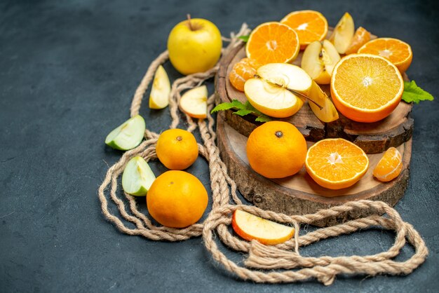 Vue de dessus des pommes et des oranges coupées sur un cocktail de planche de bois sur fond sombre