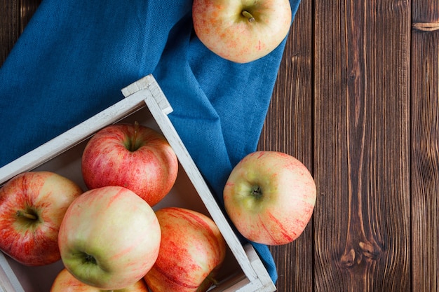 Vue de dessus des pommes rouges dans une boîte en bois et autour sur tissu bleu et fond en bois. horizontal