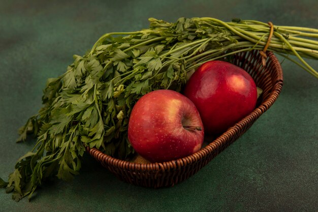 Vue de dessus des pommes rouges et douces fraîches et du persil sur un seau sur fond vert