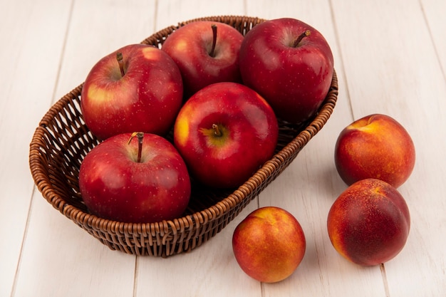 Vue de dessus des pommes rouges douces sur un seau avec des pêches isolé sur un mur en bois blanc