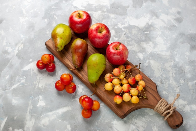 Photo gratuite vue de dessus des pommes rouges fraîches avec des cerises douces, des prunes et des poires sur un bureau blanc clair.