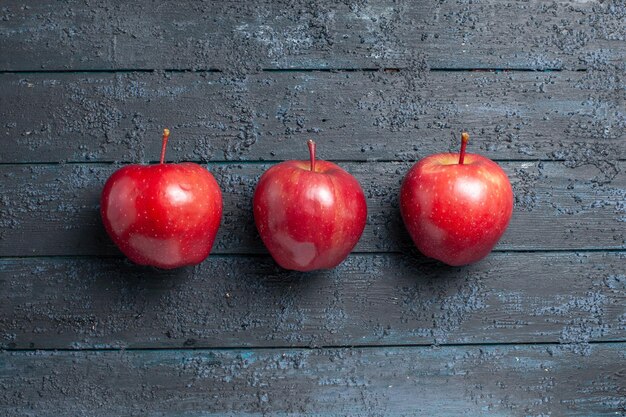 Vue de dessus des pommes rouges fraîches, des fruits mûrs et moelleux bordés sur le bureau bleu foncé de nombreux fruits rouges de couleur fraîche plante d'arbre