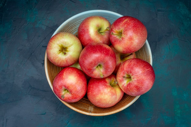 Vue de dessus pommes rouges fraîches juteuses et moelleuses à l'intérieur de la plaque sur le bureau bleu foncé fruits frais mûrs doux vitamine