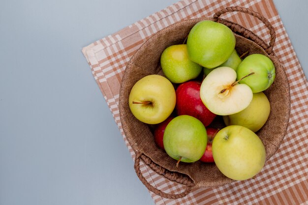 Vue de dessus des pommes rouges jaunes vertes dans le panier sur tissu à carreaux et fond gris avec espace copie