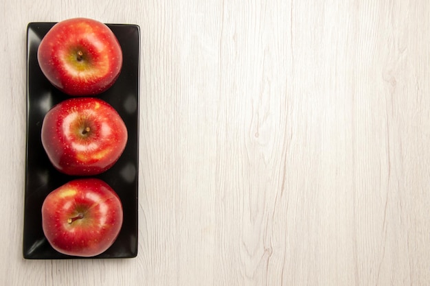 Vue de dessus pommes rouges moelleuses fruits frais à l'intérieur d'une casserole noire sur un bureau blanc fruits mûrs mûrs couleur rouge frais