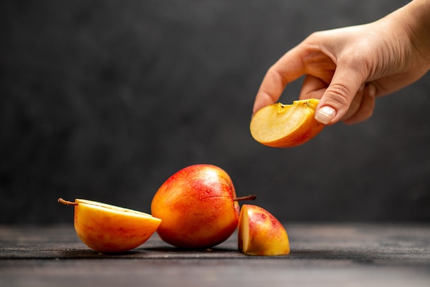 Vue de dessus de pommes rouges naturelles fraîches hachées et entières prenant l'un des citrons verts sur fond noir