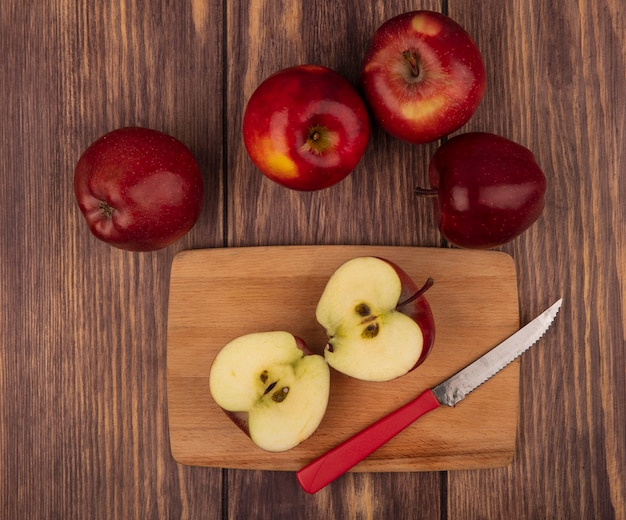 Photo gratuite vue de dessus des pommes rouges saines sur une planche de cuisine en bois avec un couteau avec des pommes isolé sur un mur en bois