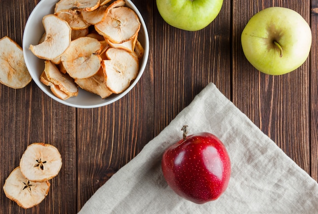 Vue de dessus des pommes séchées dans un bol avec des pommes fraîches sur un tissu et un fond en bois. horizontal