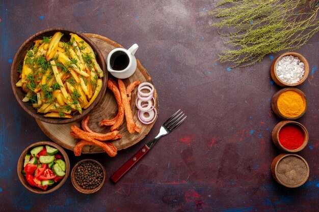 Vue de dessus des pommes de terre frites avec des assaisonnements et différents légumes sur une surface sombre