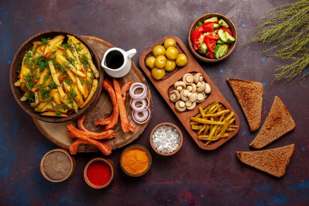 Vue de dessus des pommes de terre frites avec des assaisonnements, des miches de pain et différents légumes sur la surface sombre