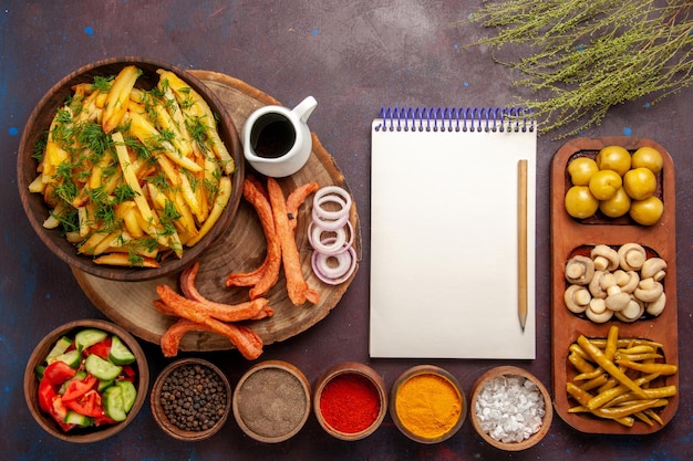 Vue de dessus des pommes de terre frites avec du pain d'assaisonnement et différents légumes sur le bureau sombre