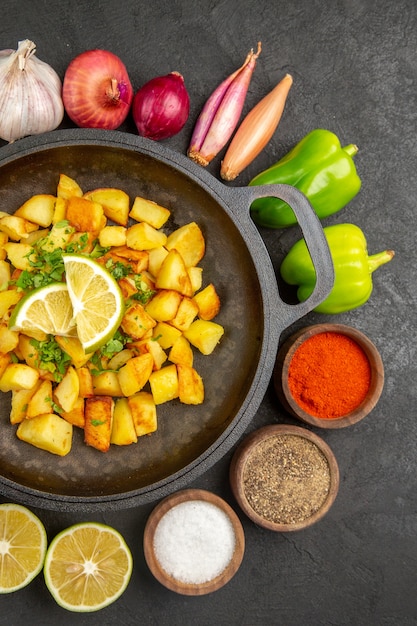 Vue de dessus des pommes de terre frites à l'intérieur de la casserole avec différents assaisonnements et légumes sur fond sombre