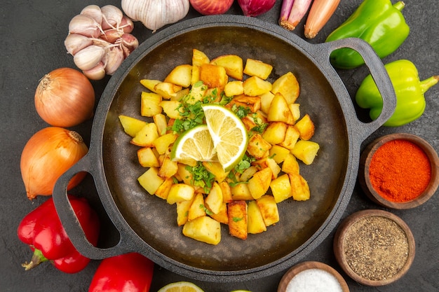 Vue de dessus des pommes de terre frites à l'intérieur de la casserole avec différents assaisonnements et légumes sur fond sombre