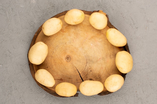 Vue de dessus des pommes de terre pelées fraîches sur le bureau brun et le sol gris