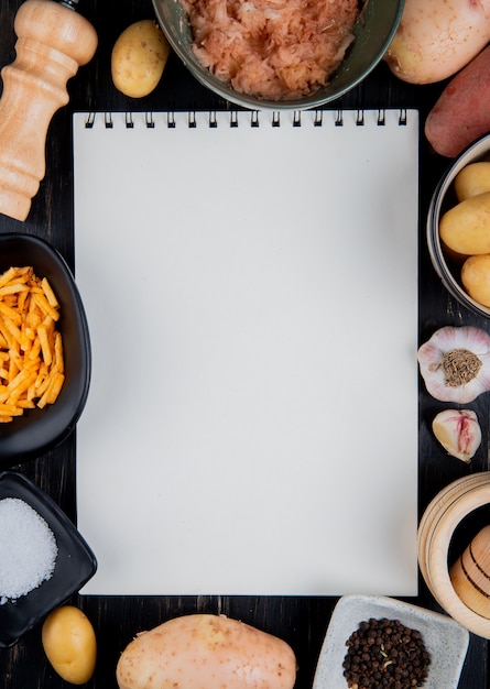 Vue de dessus de pommes de terre râpées et entières autour de bloc-notes avec du sel poivre noir sur une surface en bois avec copie espace