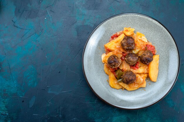 Vue de dessus pommes de terre en tranches cuites avec des boulettes de viande à l'intérieur de la plaque sur fond bleu foncé.