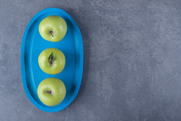 Vue de dessus des pommes vertes biologiques fraîches sur planche de bois bleue.