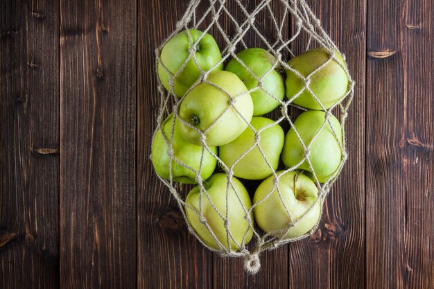 Vue de dessus des pommes vertes dans un sac net et autour sur fond de bois. espace horizontal pour le texte