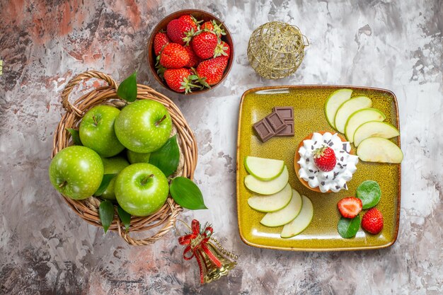 Vue de dessus des pommes vertes tranchées avec des fraises et des gâteaux sur fond clair