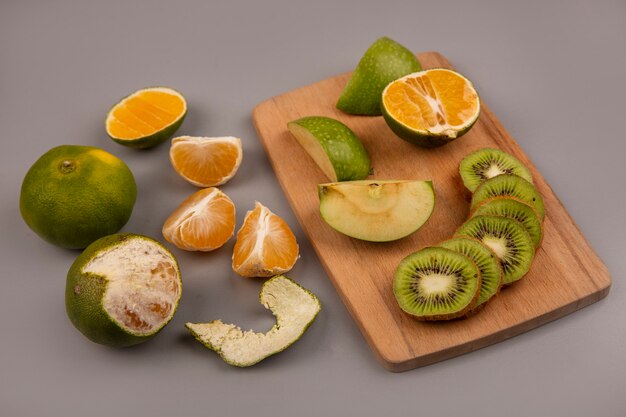 Vue de dessus des pommes vertes avec des tranches de kiwi sur une planche de cuisine en bois avec des mandarines isolées