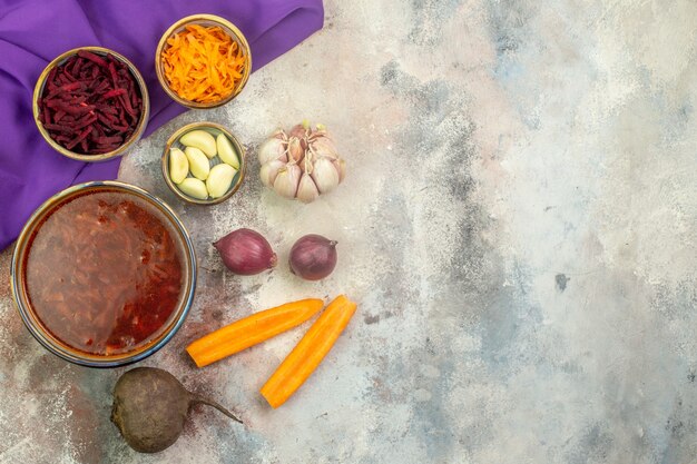 Vue de dessus d'un pot avec une délicieuse soupe de bortsch et une cuillère en bois de différents légumes sur une serviette bleu violet sur fond coloré