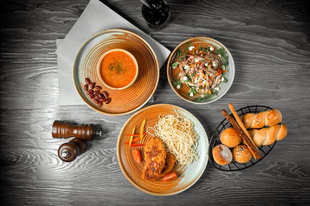 Vue de dessus première salade de soupe aux lentilles et plat principal avec des pâtes et une boisson gazeuse sur la table