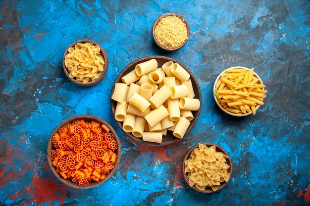 Vue de dessus de la préparation du dîner avec des nouilles de pâtes dans des pots de différentes tailles sur fond bleu