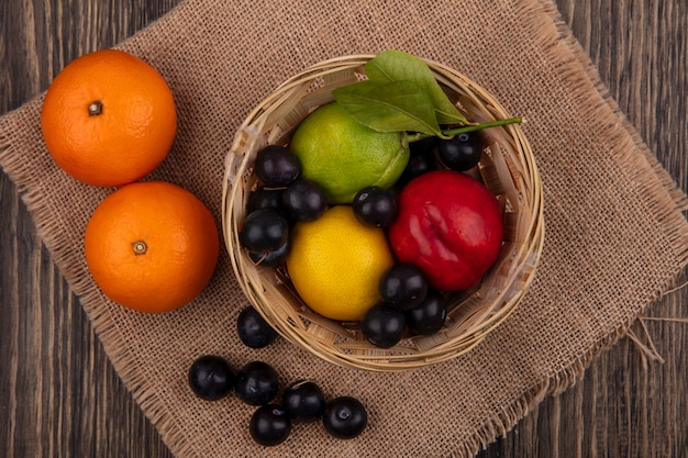 Vue de dessus prune cerise avec citron lime et pêche dans un panier avec des oranges sur une serviette beige