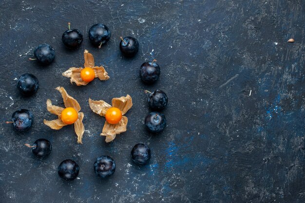 Vue de dessus des prunelles fraîches bordées de cercle sur un bureau sombre, vitamine alimentaire de baies de fruits frais