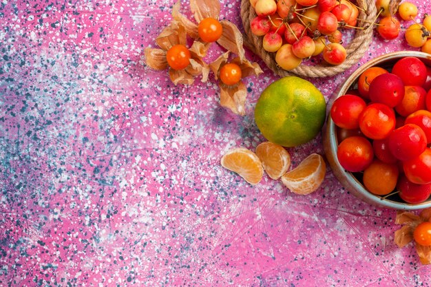 Vue de dessus prunes aigres fraîches fruits moelleux à l'intérieur de petite assiette avec cerises et mandarine sur le bureau rose.