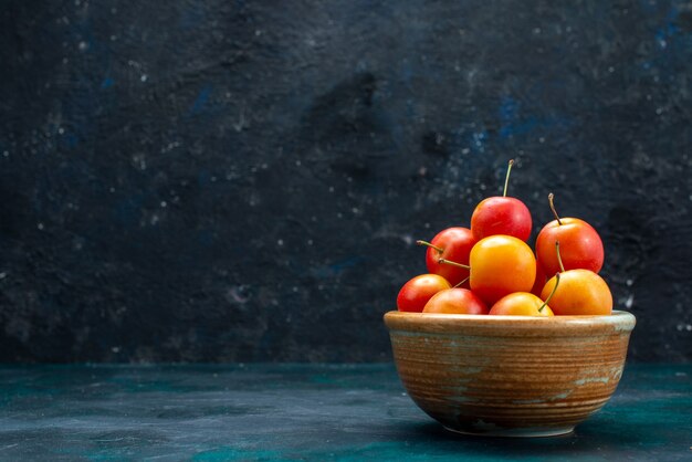 Vue de dessus des prunes de cerises fraîches fruits aigres et moelleux à l'intérieur de petit pot sur le fond bleu foncé fruits doux frais vitamine