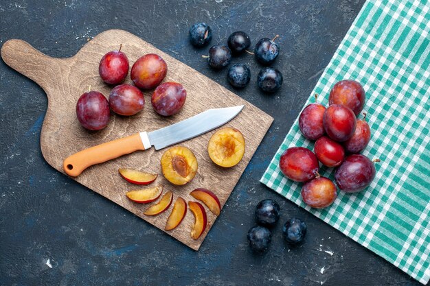 Vue de dessus des prunes fraîches entières moelleuses et juteuses tranchées sur un bureau sombre, fruits frais d'été