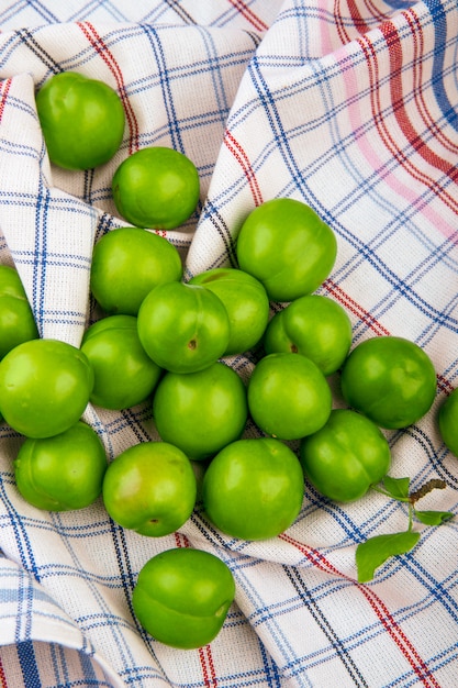Photo gratuite vue de dessus des prunes vertes aigres éparpillées sur une table en tissu à carreaux