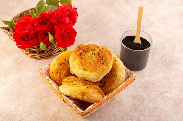 Une vue de dessus qogals cuits au four petits pains cuits au four frais chaud à l'intérieur du bac à pain avec des fleurs rouges et du poivre sur table et rose
