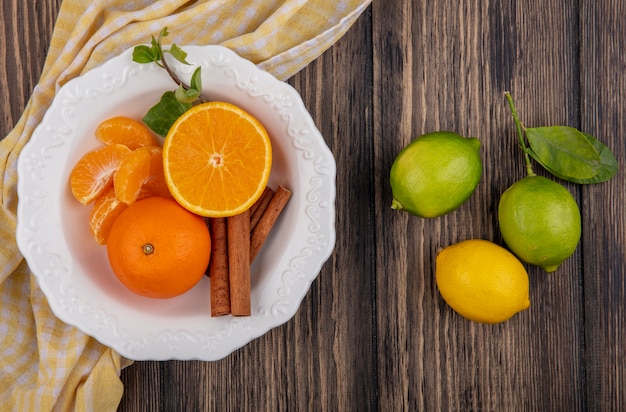 Photo gratuite vue de dessus des quartiers d'orange pelées avec de la cannelle dans une assiette et du citron avec des limes sur fond de bois