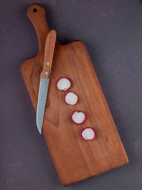 Vue de dessus des radis coupés et couteau sur une planche à découper sur fond marron avec espace copie