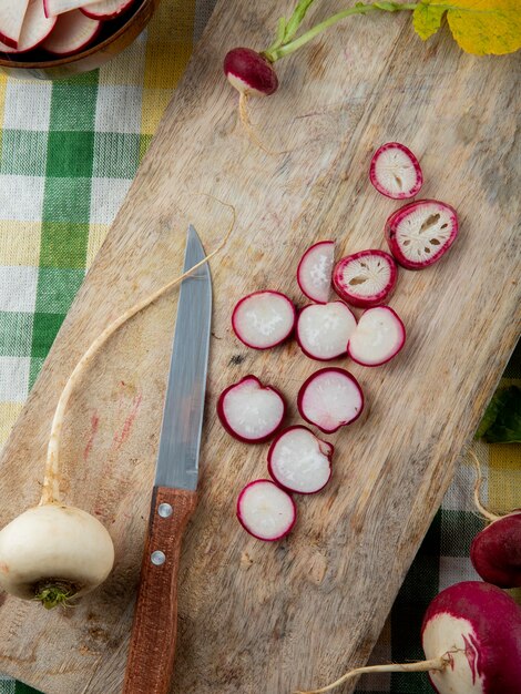 Vue de dessus des radis rouges en tranches et des radis blancs sur une planche à découper avec un couteau sur fond de tissu