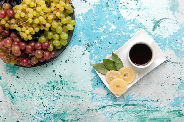 Vue de dessus des raisins colorés frais fruits juteux et moelleux avec une tasse de thé sur fond bleu clair fruits baies vin de jus de fruits frais et moelleux