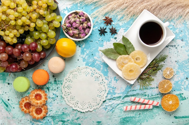 Vue de dessus des raisins de couleur fraîche avec une tasse de thé sur la surface bleu clair fruits cookies sucre gâteau sucré cuire la tarte