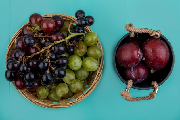 Vue de dessus des raisins dans le panier et bol de pluots sur fond bleu