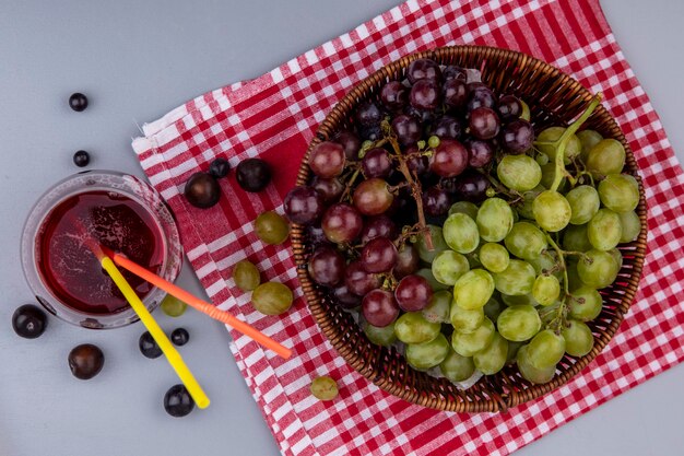 Vue de dessus des raisins dans le panier sur tissu à carreaux et verre de jus de raisin sur fond gris