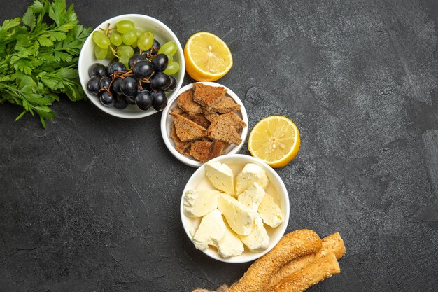 Vue de dessus des raisins frais et moelleux avec du fromage blanc et du pain tranché sur une surface sombre, des fruits au lait