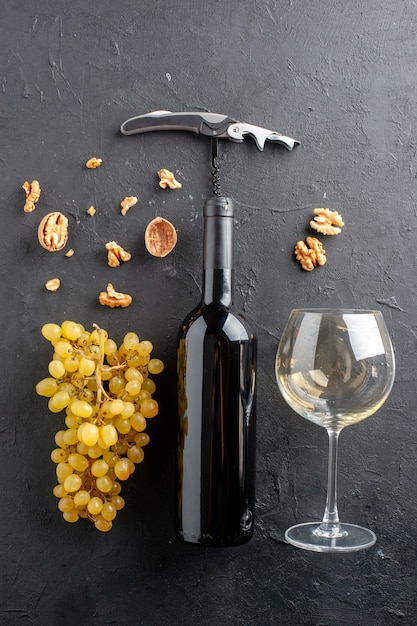 Photo gratuite vue de dessus raisins jaunes frais noyer bouteille et ouvre-vin en verre sur table sombre