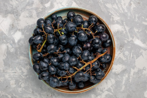 Vue de dessus raisins noirs frais juteux fruits sucrés moelleux sur le bureau blanc clair